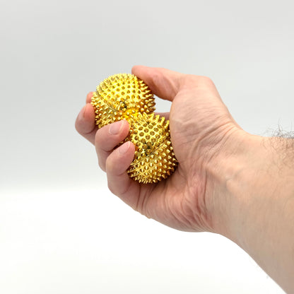 Zwei goldene Akupressur Magnetbälle in der Hand – Handmassage & Fidget Toy für Anspannungsabbau