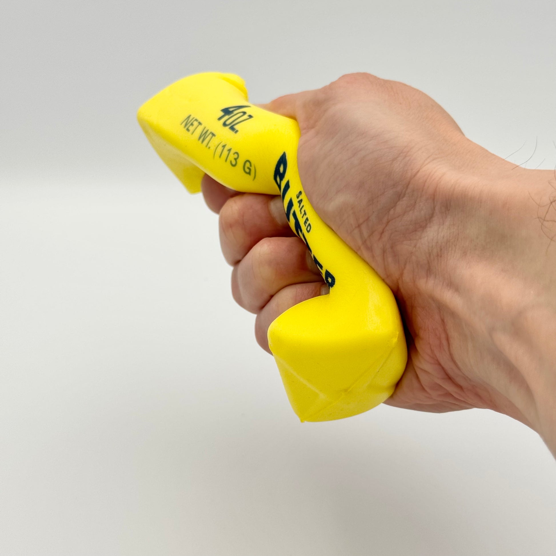 Gelber Butter-Antistressball in Form eines Butterstücks wird in der Hand gedrückt – Squeezy Fidget Toy