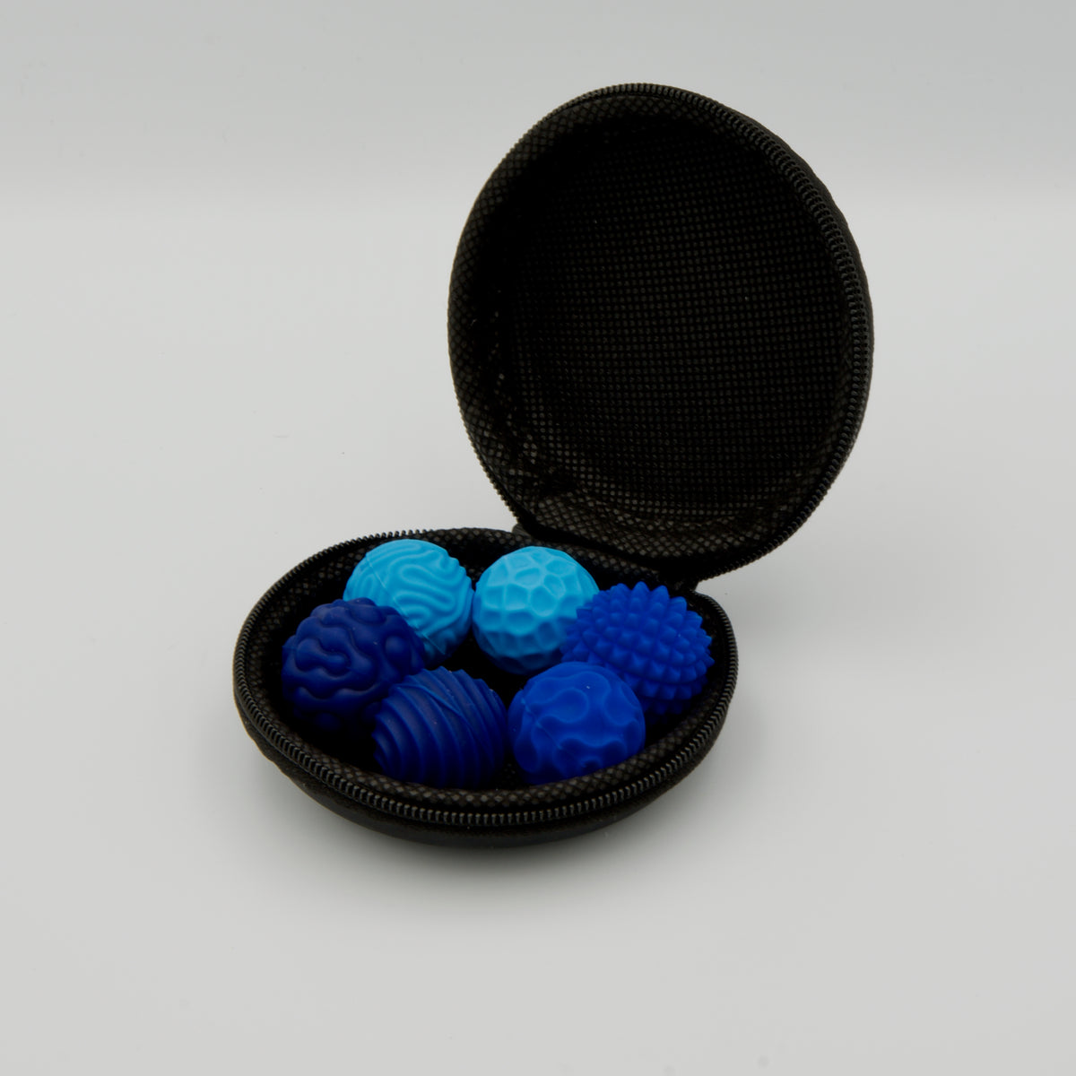 Geöffnetes, schwarzes Rund-Etui gefüllt mit sechs blauen Haptik-Bällen mit unterschiedlichen Oberflächenstrukturen