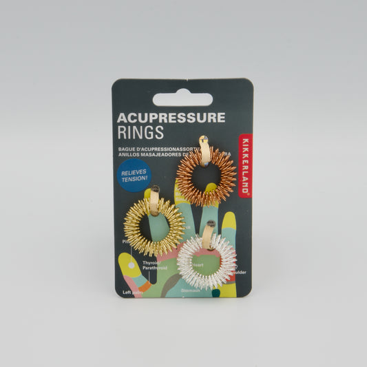 Kikkerland Verpackung mit drei Akupressur-Fingeringen aus elastischem Draht in Gold, Silber und Bronzefarbe.