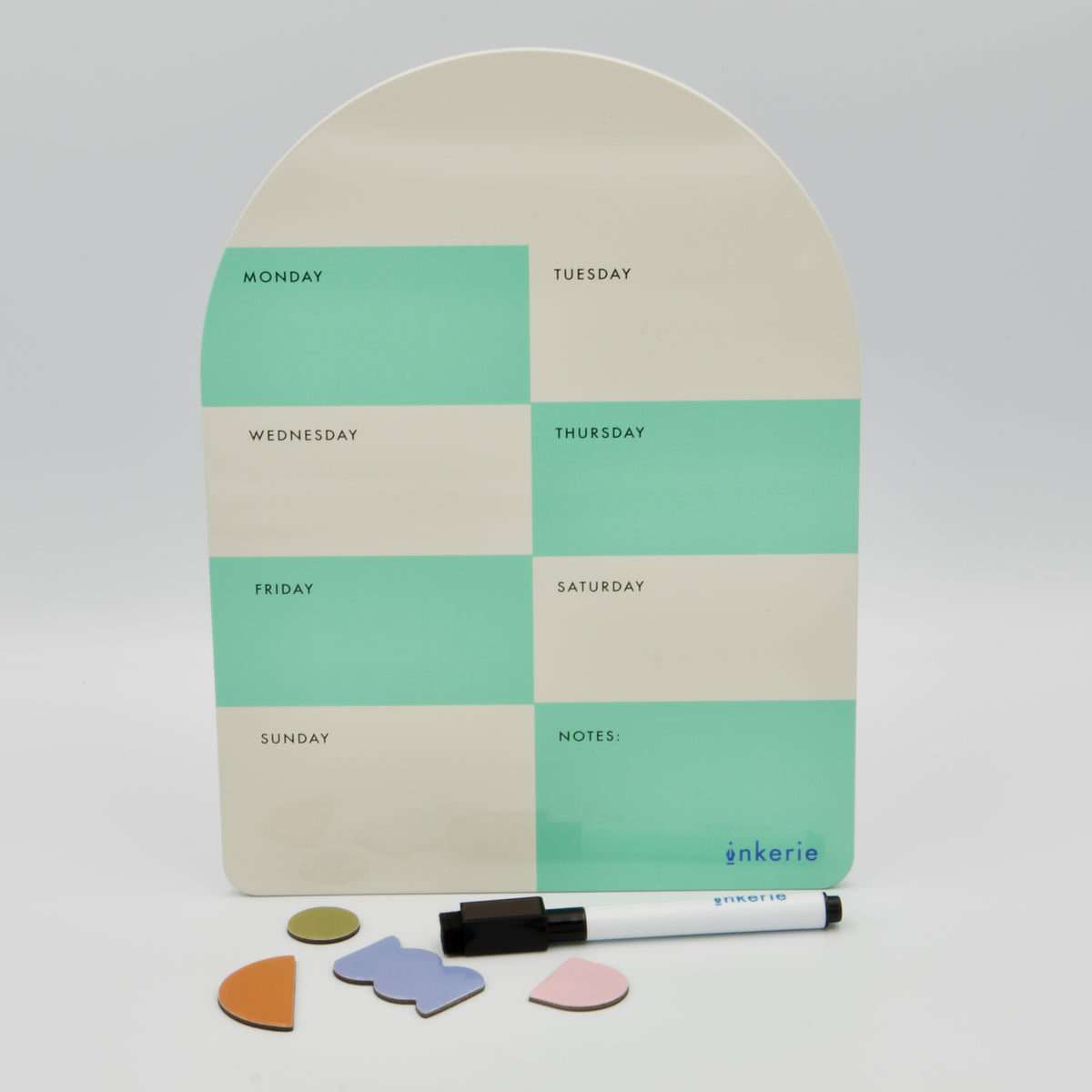 Bogenförmige magnetische Wochenplaner-Tafel von inkerie in Mintgrün und Beige mit Stift und vier bunten Formmagneten davor.