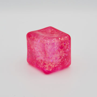 Glitzernder, pinkfarbener Quetschwürfel mit dichter Füllung auf hellem Untergrund