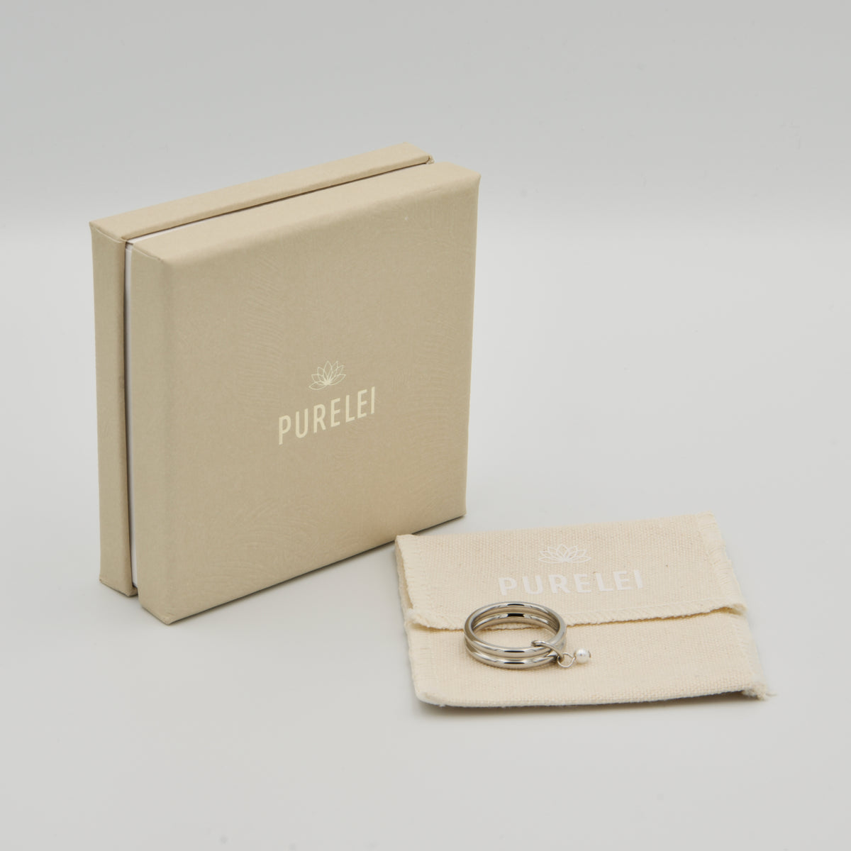 Beigefarbene PURELEI Schmuckverpackung und Stoffbeutel mit einem silbernen Ring und Perlenanhänger
