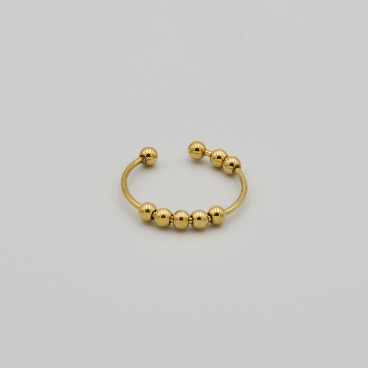 Offener, goldfarbener Fidget-Schmuckring mit mehreren frei beweglichen Metallkugeln auf hellem Hintergrund