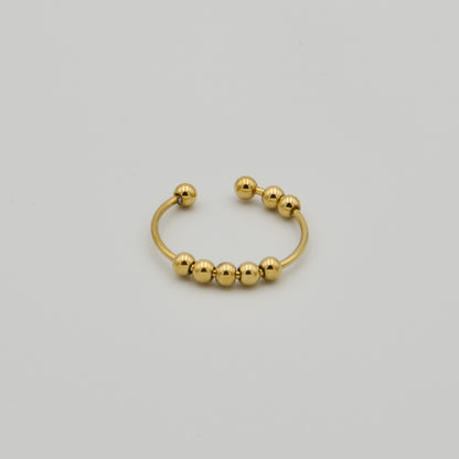 Offener, goldfarbener Fidget-Schmuckring mit mehreren frei beweglichen Metallkugeln auf hellem Hintergrund