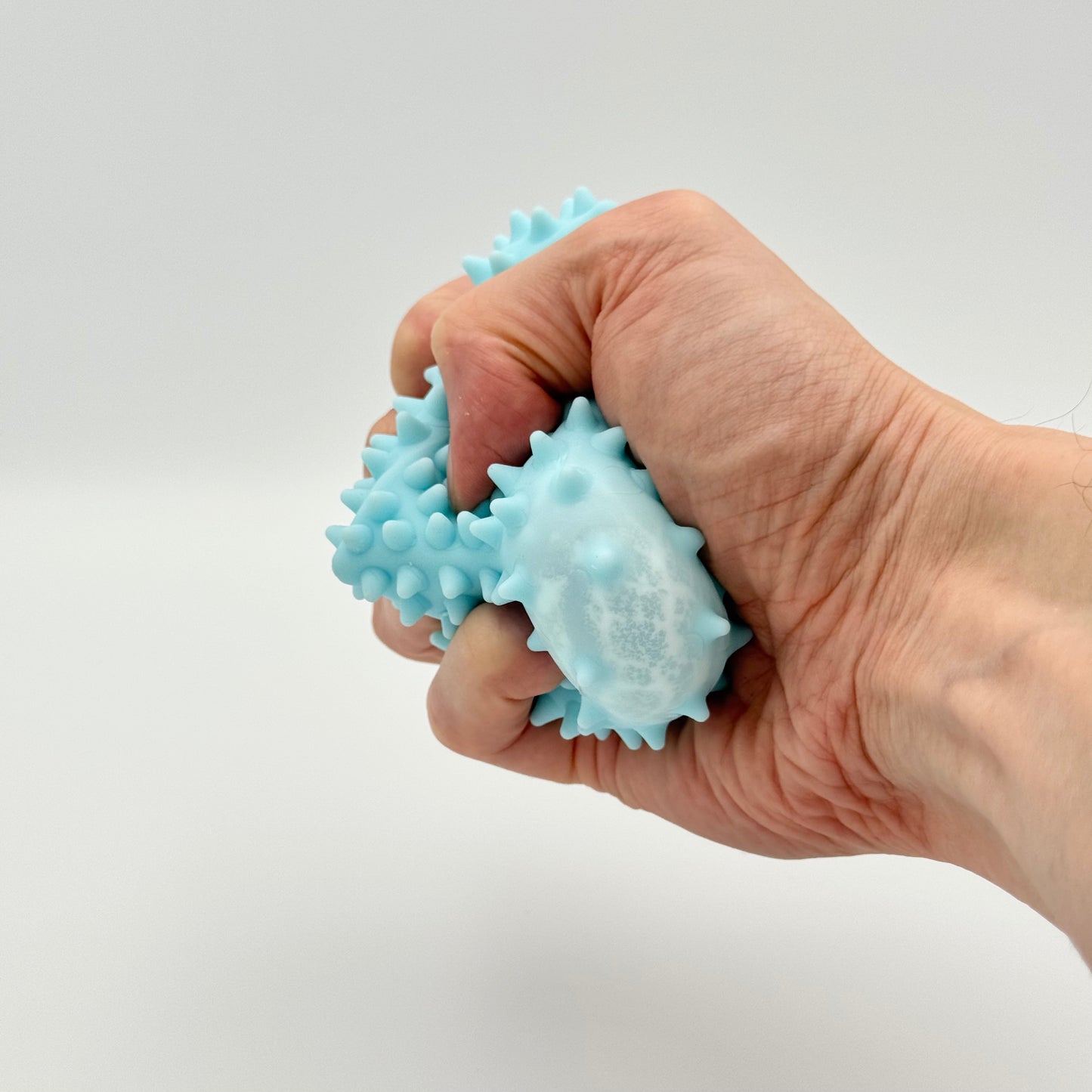 Hellblauer Pyramiden-Anti-Stressball mit Noppen wird geknetet – Taktiler Squeezy Ball