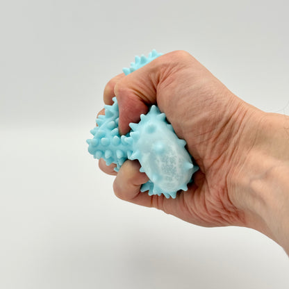 Hellblauer Pyramiden-Anti-Stressball mit Noppen wird geknetet – Taktiler Squeezy Ball