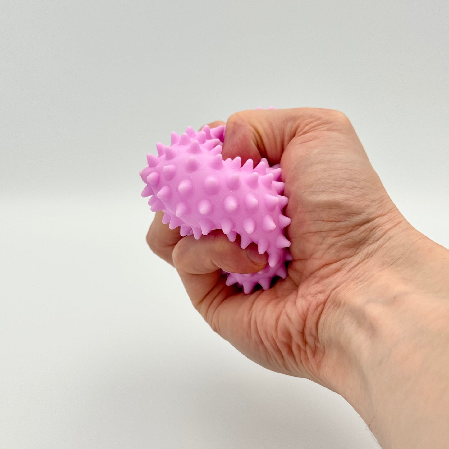 Lila Pyramiden-Anti-Stressball mit Noppen in der Hand gedrückt – Squeezy Skill Tool