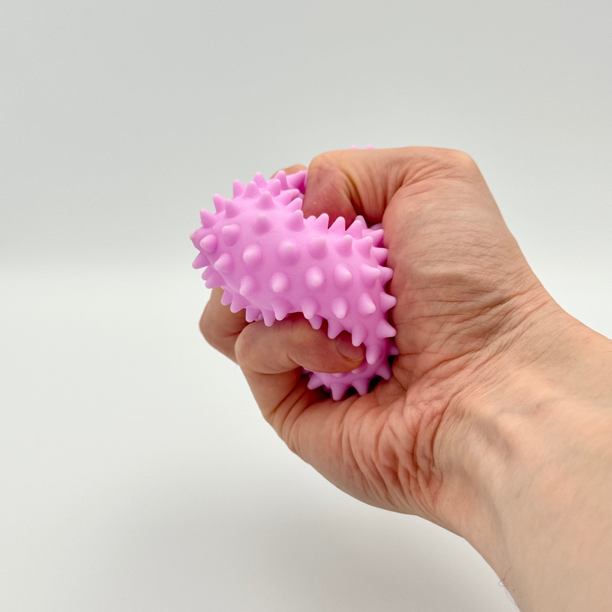 Lila Pyramiden-Anti-Stressball mit Noppen in der Hand gedrückt – Squeezy Skill Tool