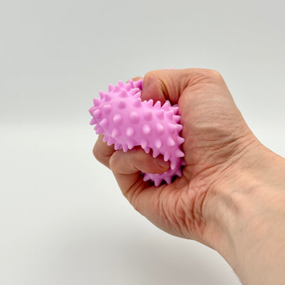 Lila Pyramiden-Anti-Stressball mit Noppen in der Hand gedrückt – Squeezy Skill Tool