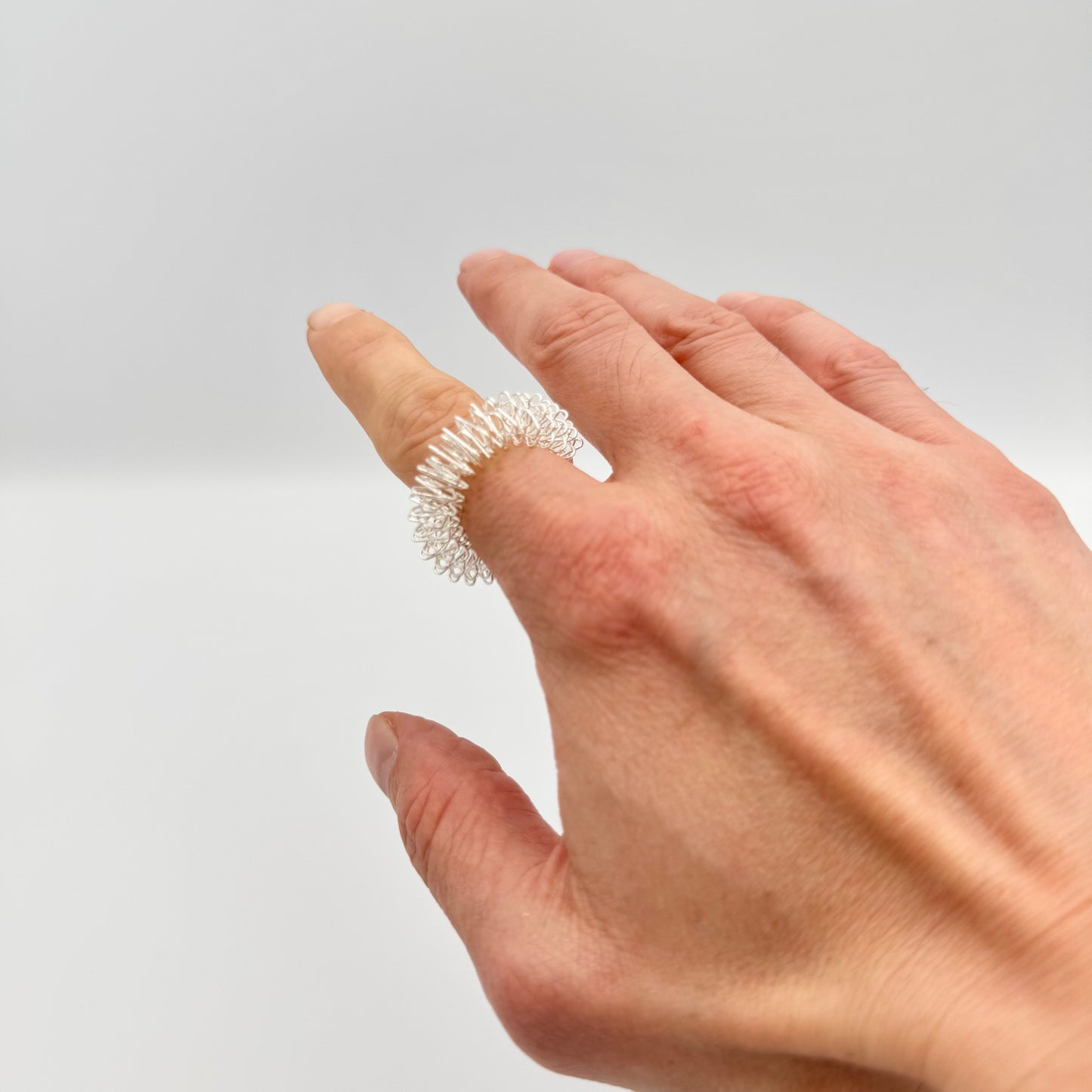 Silberner Therastar Fingermassagering wird am Finger abgerollt – DBT Akupressurring für Haptik