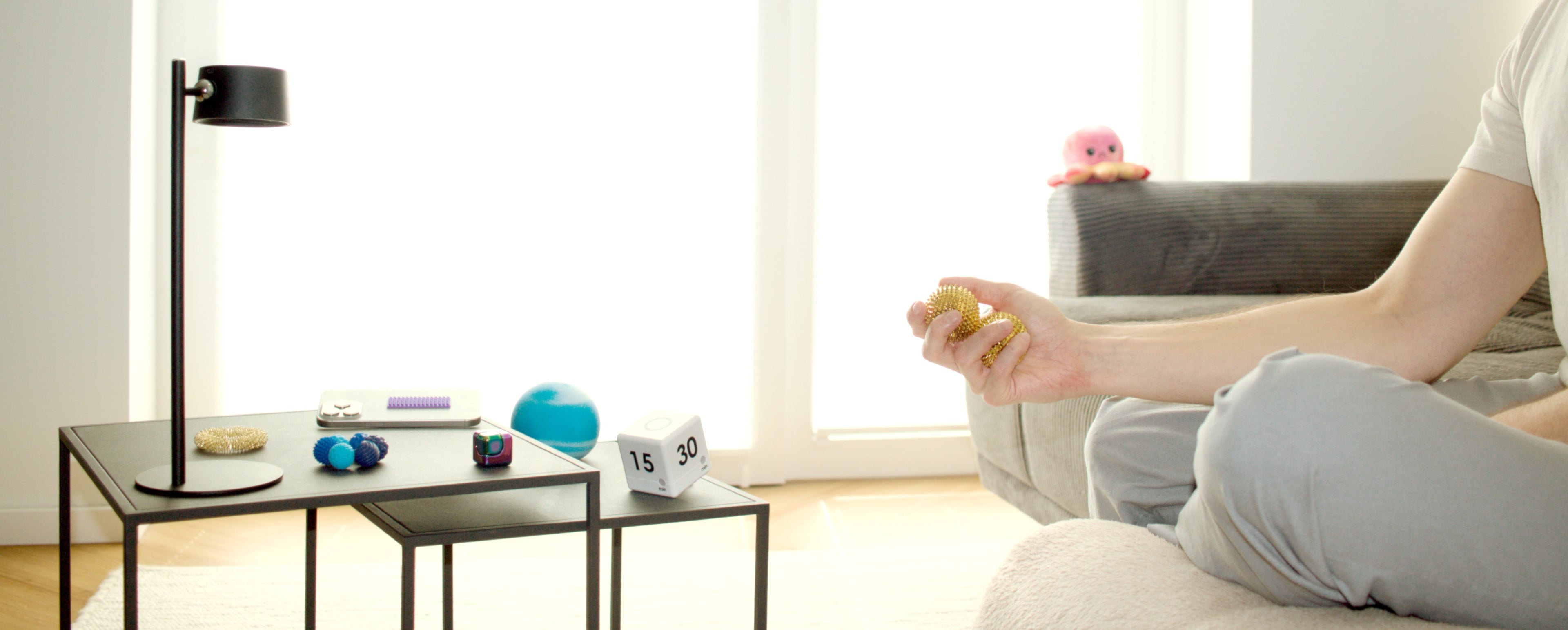 Person nutzt goldene Akupressurbälle zur Entspannung auf dem Sofa – Beistelltisch mit verschiedenen Fidget Toys & Skills